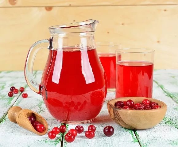 Клюквенный морс в графине и стаканах и ягоды клюквы на столе и в чашке